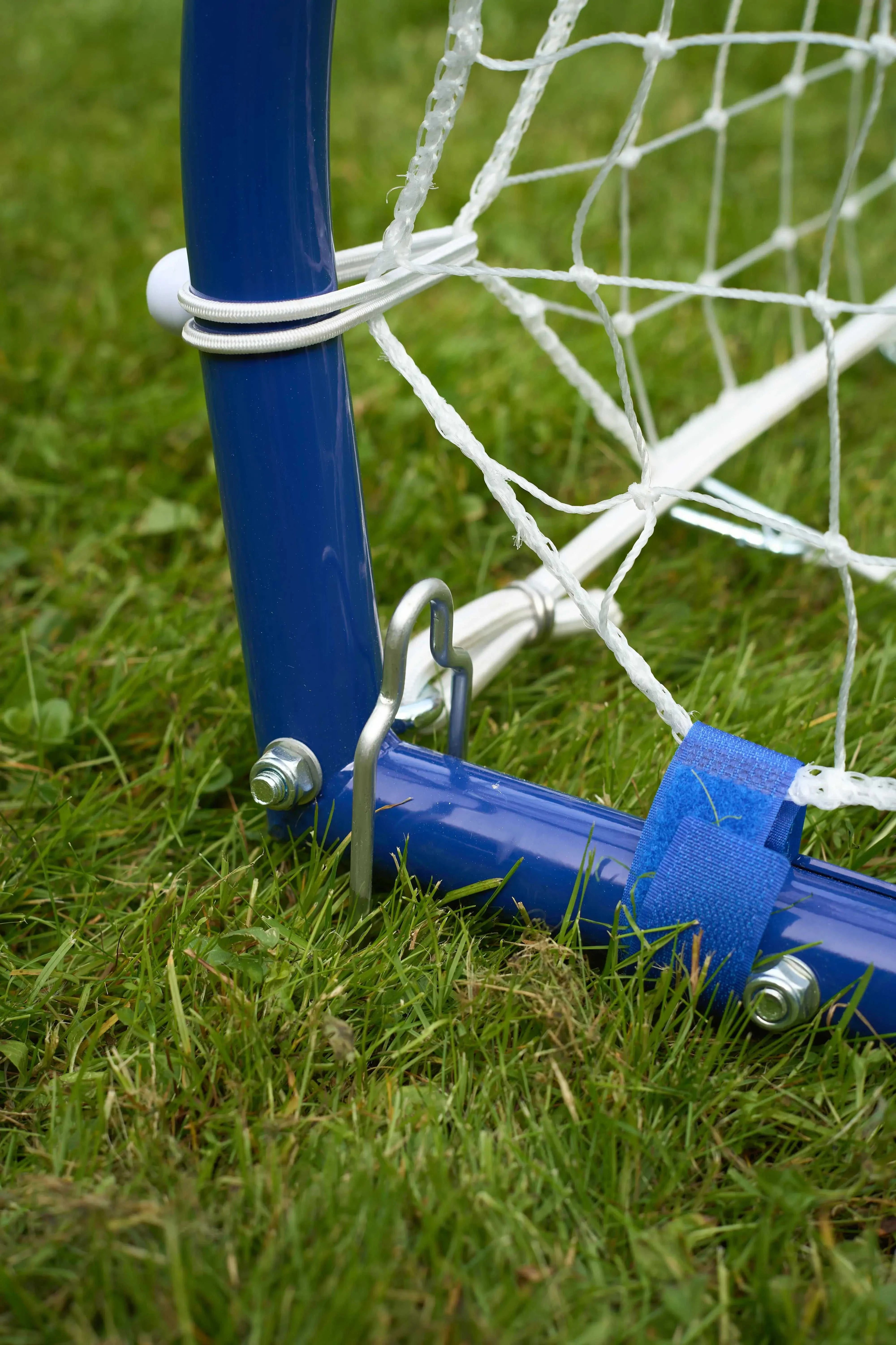 Close-up of the durable metal frame and net attachment of a football rebounder goal trainer on grass.